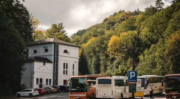 Autobusy czekają przed Starą Kruszarnią w Złotym Stoku. Jesienne drzewa otaczają parking.