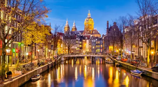 Wieczorne atrakcje Amsterdamu: malowniczy kanał z odbijającymi się światłami, most, rowery i zabytkowa architektura.