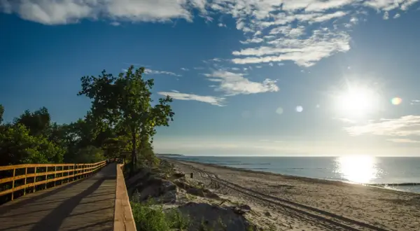 Drewniana kładka wzdłuż plaży, idealna na spacer. Słońce odbija się w morzu, tworząc malowniczą r10 trasę.