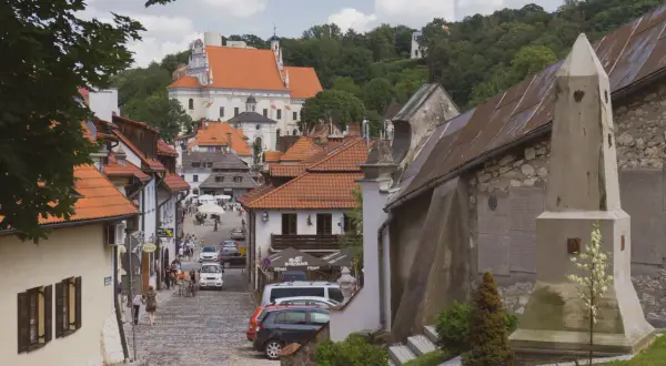 Urokliwa ulica w Kazimierzu Dolnym z kościołem na wzgórzu. Kamienne bruki, kamienice z czerwonymi dachami i zielone drzewa tworzą malowniczy krajobraz.