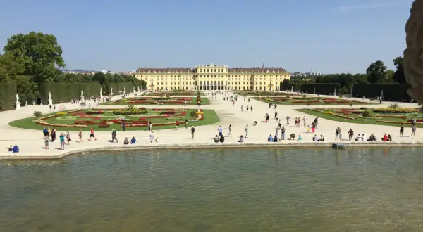 Piękny park w Wiedniu z pałacem w tle i ludźmi spacerującymi po kwiecistych rabatach.
