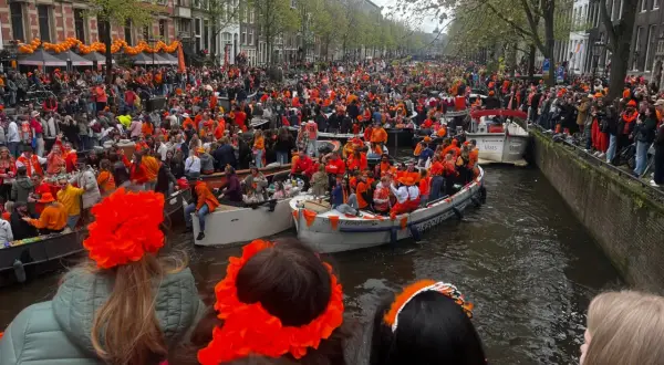 Tłumy ludzi w pomarańczowych strojach świętują dzień króla w Amsterdamie, płynąc łodziami po kanałach.