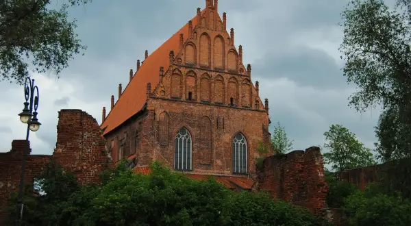 Gotycka ceglana bazylika z czerwonym dachem, ruiny murów obronnych i zieleń. To jedno z miejsc, co zobaczyć w Elblągu.
