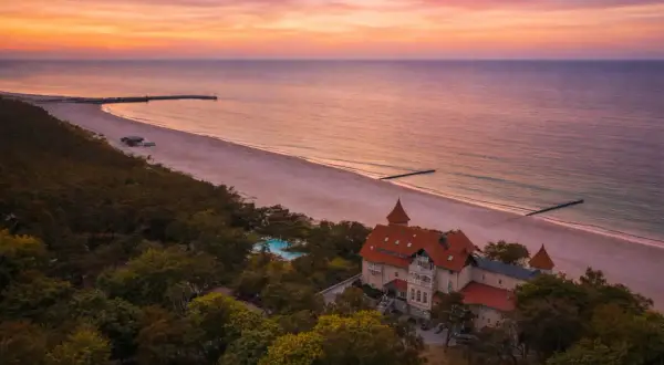 Piękny zachód słońca nad morzem, z widokiem na hotel i plażę. Idealne miejsce, by zastanowić się, gdzie na wakacje.