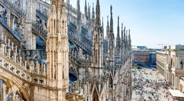 Majestatyczne iglice katedry Duomo w Mediolanie w marcu, z tłumem ludzi spacerującym po placu poniżej.