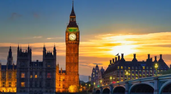 Wieża zegarowa Big Ben w Londynie o zachodzie słońca, z Parlamentem i mostem w tle.