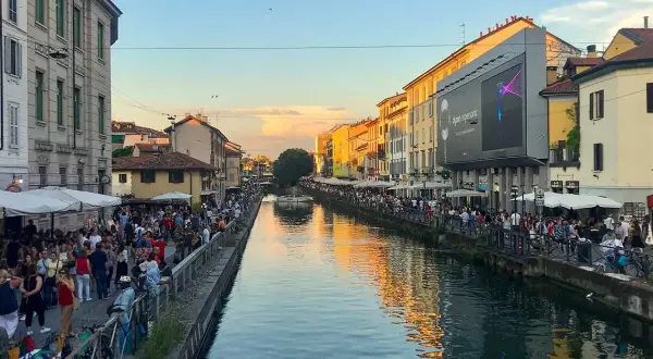 Tętniące życiem Navigli w Mediolanie. Ludzie spacerują wzdłuż kanału, ciesząc się wieczornym słońcem i atmosferą.