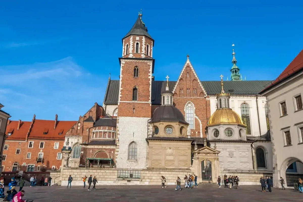 Majestatyczna katedra wawelska z cegły i kamienia, z dominującą wieżą i złotą kopułą, na tle błękitnego nieba.