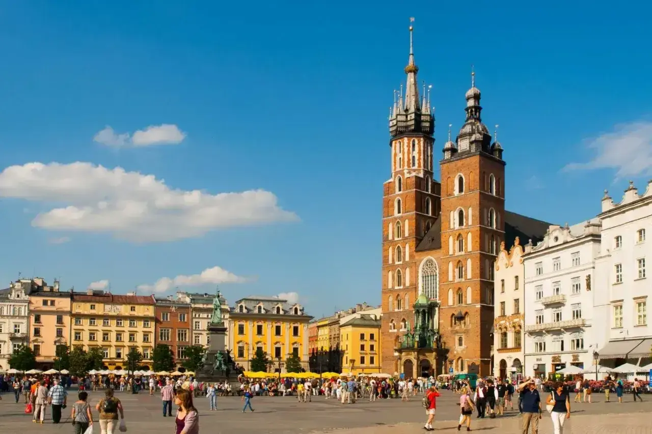 Rynek Główny w Krakowie tętni życiem. W tle Bazylika Mariacka i kolorowe kamienice.