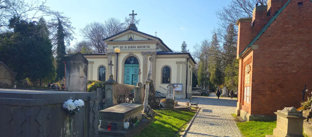 Cmentarz Rakowicki, z kaplicą i nagrobkami, w słoneczny dzień.