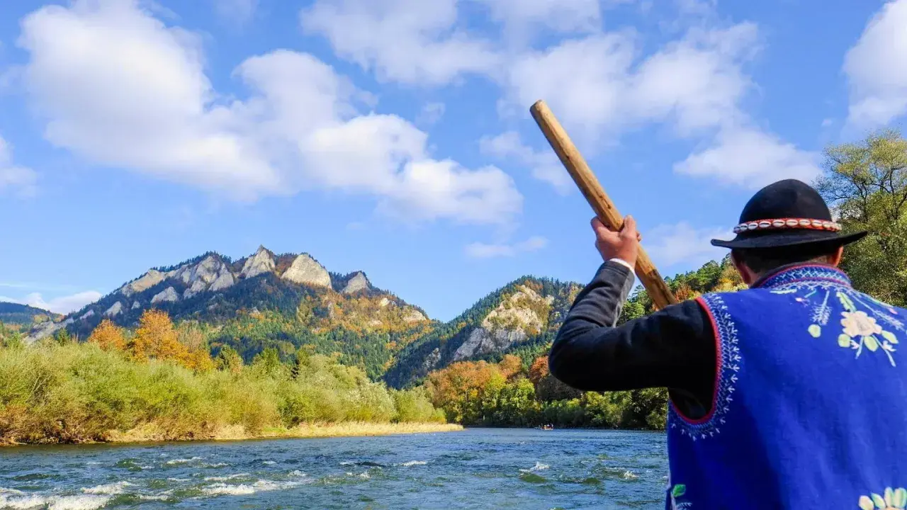 Flisacy Dunajec w tradycyjnych strojach płyną tratwą przez malowniczy przełom rzeki. Góry Pieniny jesienią zachwycają kolorami.