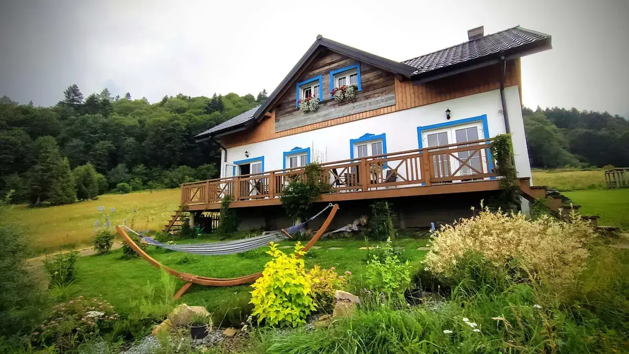 Dom z drewnianym tarasem i hamakiem w ogrodzie, otoczony zielenią. Idealne miejsce, by odpocząć i zastanowić się, gdzie w Bieszczady.