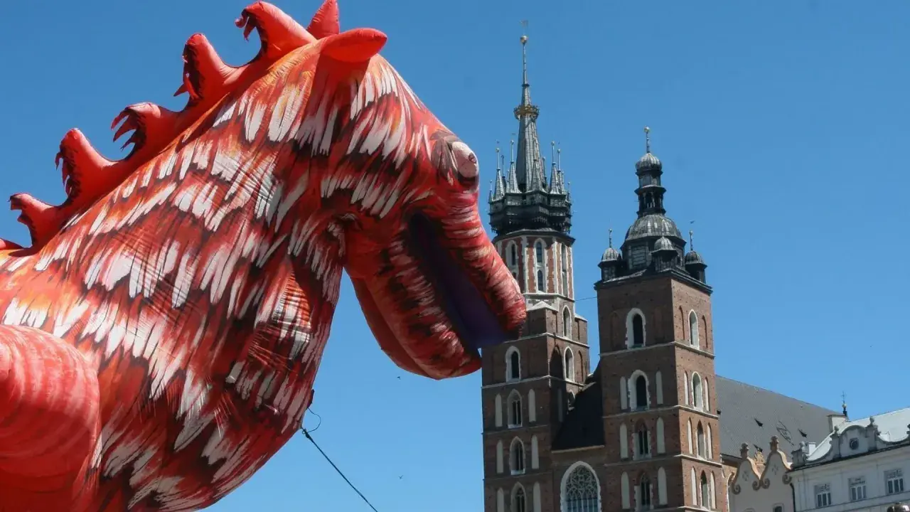 Smok wawelski, znany z atlas obscura krakow, wita turystów na tle Kościoła Mariackiego.