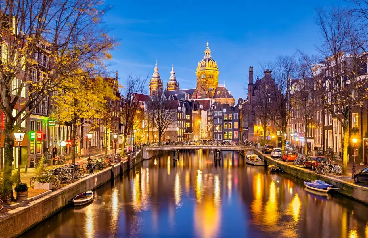 Wieczorne atrakcje Amsterdamu: malowniczy kanał z odbijającymi się światłami, most, rowery i zabytkowa architektura.