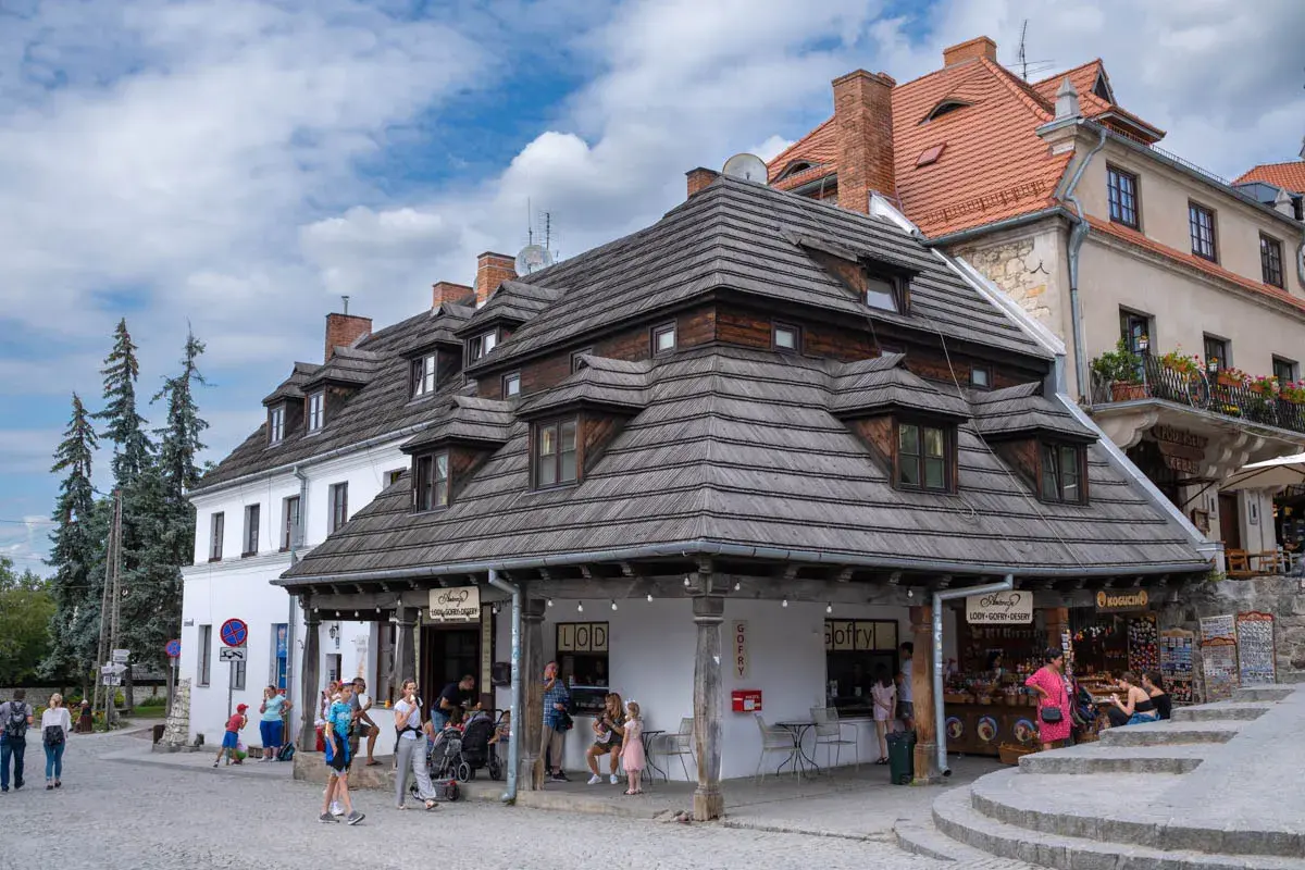 Kazimierz Dolny atrakcje: urokliwy rynek z kamieniczkami, lodziarnią i sklepikami. Ludzie spacerują, ciesząc się atmosferą.