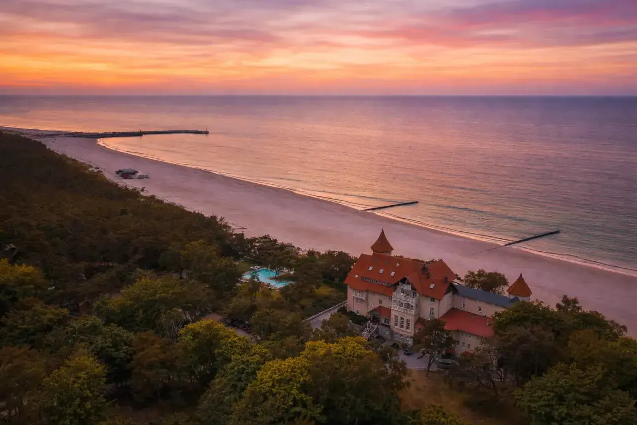 Piękny zachód słońca nad morzem, z widokiem na hotel i plażę. Idealne miejsce, by zastanowić się, gdzie na wakacje.