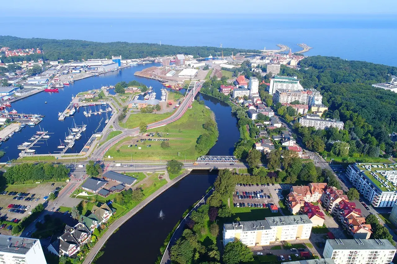 Widok z lotu ptaka na port i rzekę w Kołobrzegu. Widoczne liczne jachty, mosty, budynki mieszkalne i tereny zielone. Kołobrzeg atrakcje turystyczne w pełnej krasie.