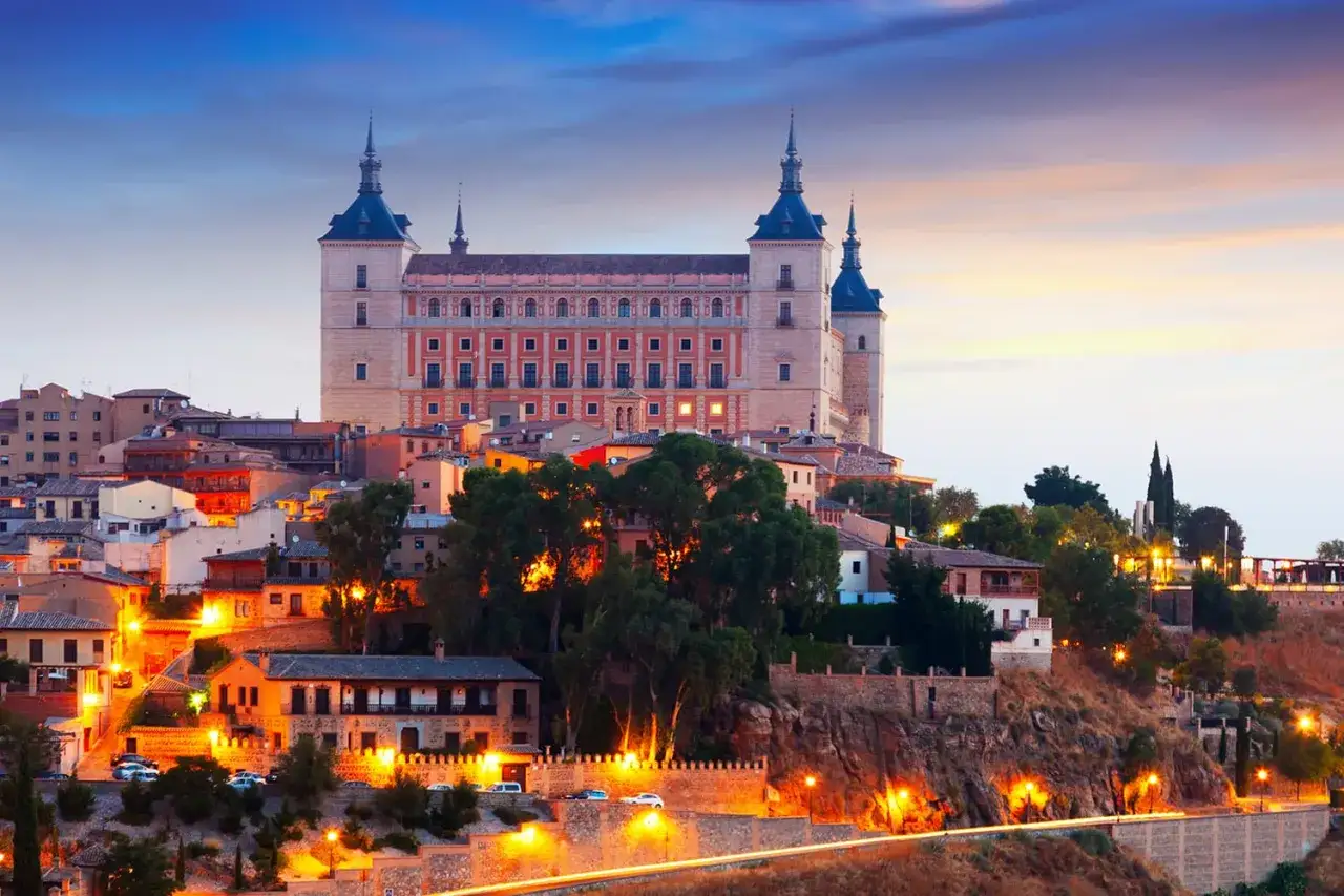 Toledo co zobaczyć: majestatyczny Alc&aacute;zar i urokliwe, oświetlone uliczki starego miasta o zmierzchu.