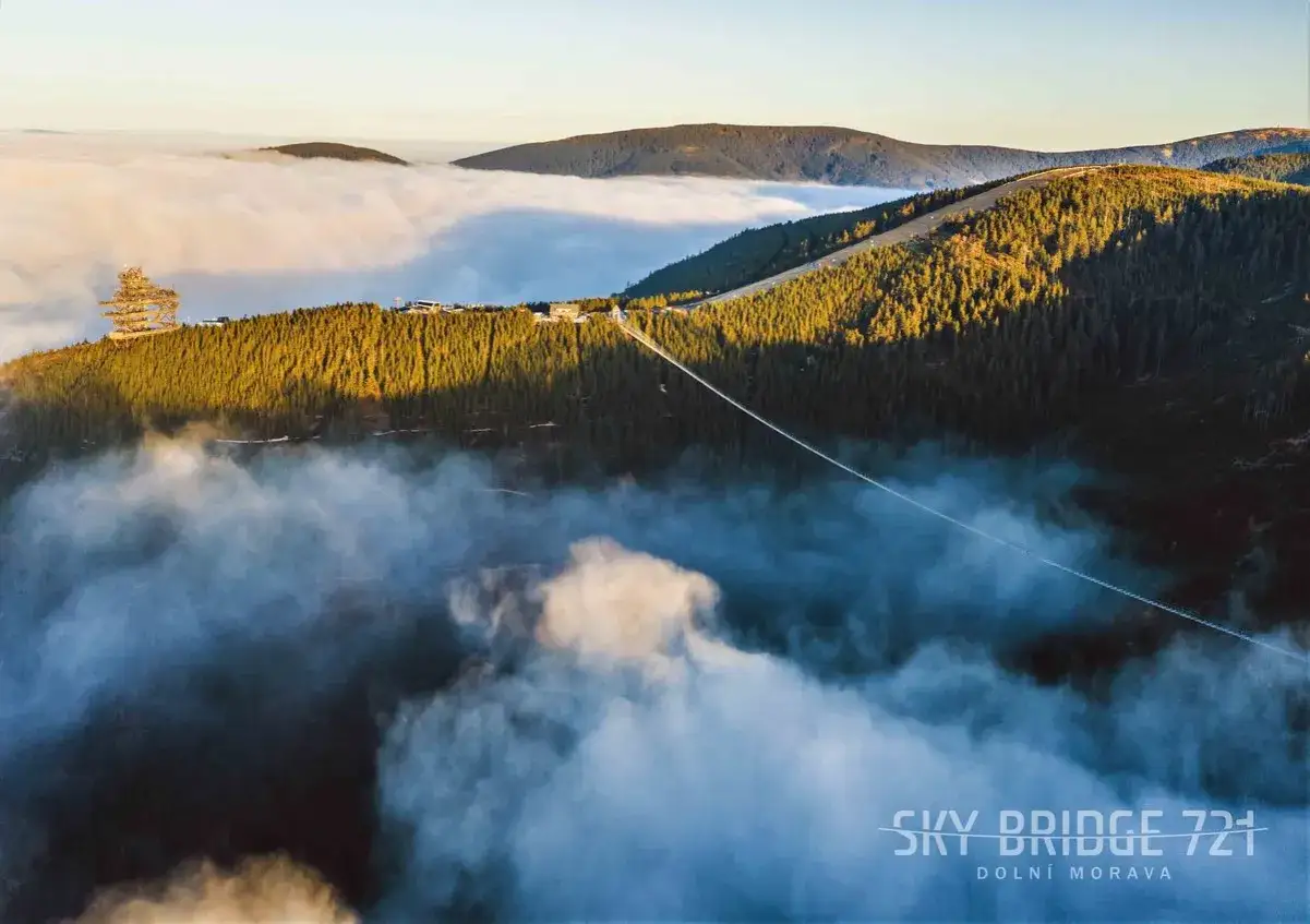 Widok na wiszący most Sky Bridge 721 w Czechach, zawieszony nad morzem chmur, otoczony lasem.