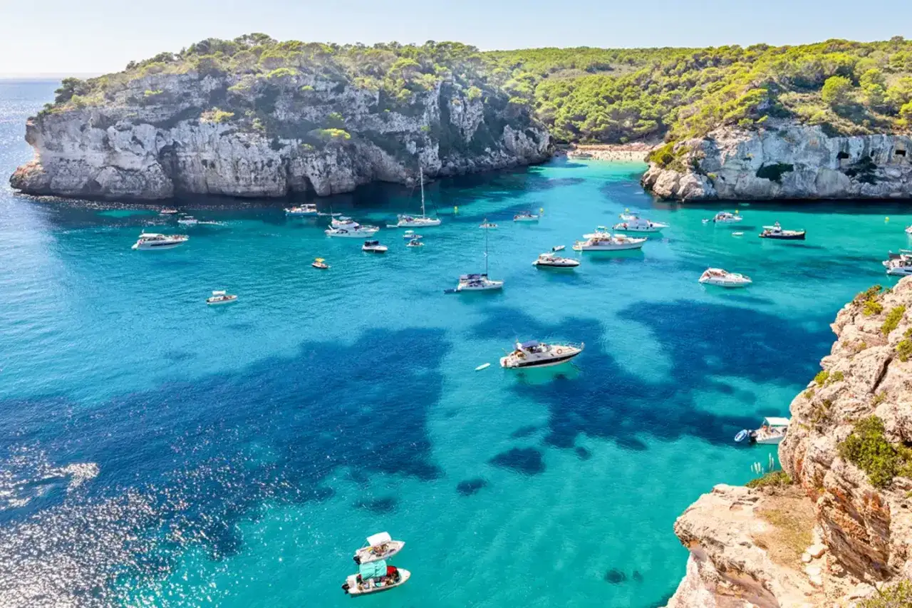 Zatoka z turkusową wodą, łodziami i klifami. Czy to Minorka czy Majorka? Piękno Balearów.
