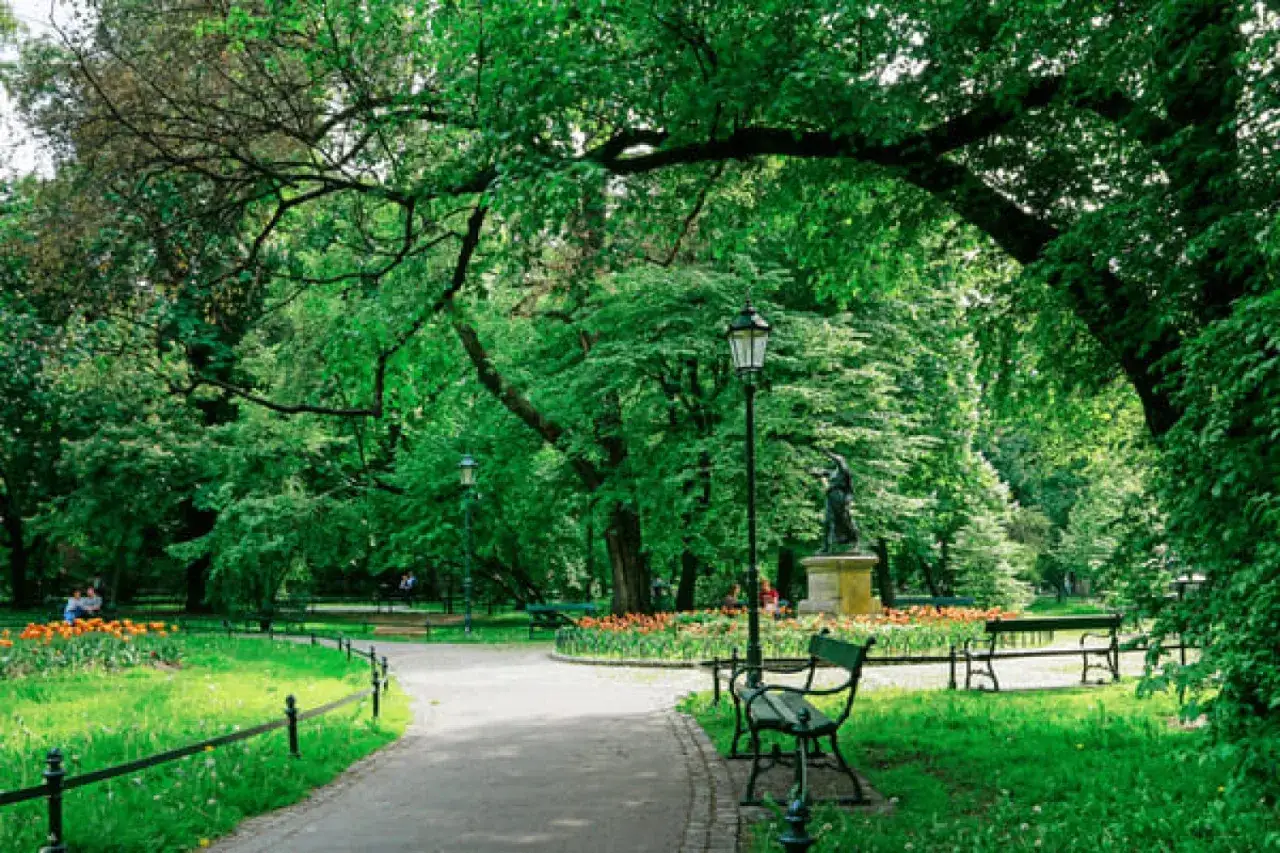 Zielony park w Krakowie, z alejkami, ławkami i rzeźbą. Idealne miejsce na spokojną niedzielę w Krakowie.