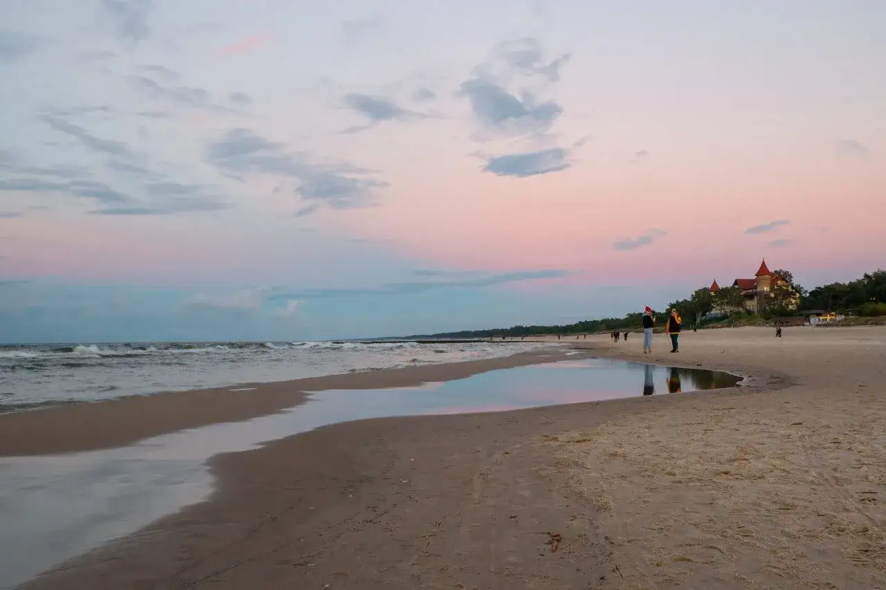 Zachód słońca nad morzem w Łebie. Spacer po plaży, odbicia w wodzie, a w oddali widać budynek. To jedne z wielu atrakcji dla dorosłych.