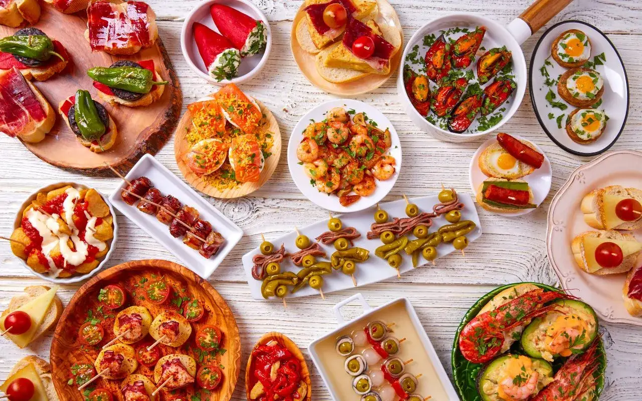 Mnóstwo pysznych tapas, czyli hiszpania jedzenie. Krewetki, małże, szynka, oliwki i wiele innych smakołyków na drewnianym stole.