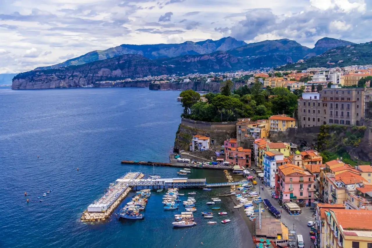 Widok na zatokę i miasteczko Sorrento z kolorowymi domami, portem pełnym łodzi i górami w tle. Idealne miejsce na odkrywanie atrakcji.