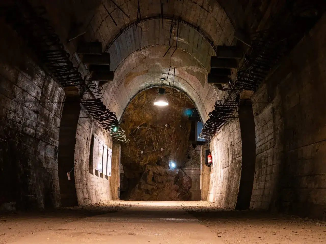 Wnętrze tunelu w Górach Sowich, gdzie kiedyś znajdowały się bunkry. Betonowe ściany, odsłonięte zbrojenia i surowe oświetlenie tworzą mroczny klimat.