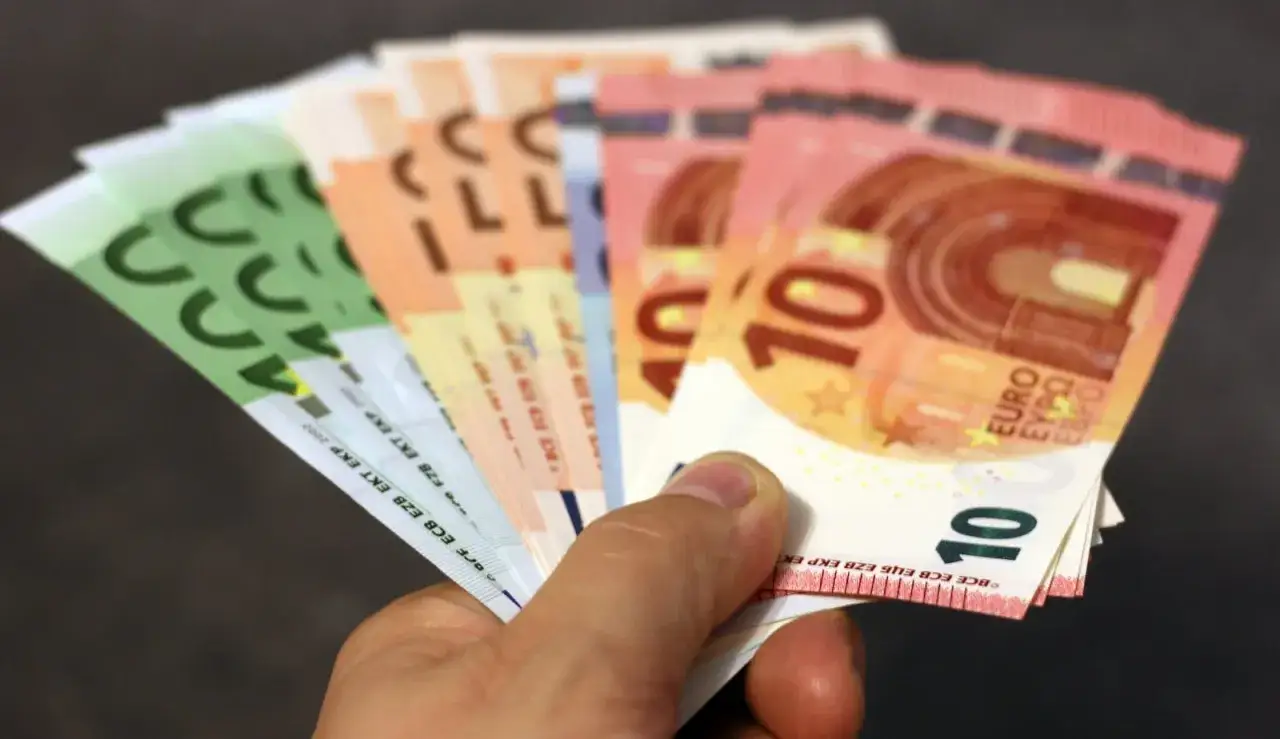 Ręka trzyma banknoty euro, które są walutą na Wyspach Kanaryjskich. Widoczne nominały to 10, 50 i 100 euro.