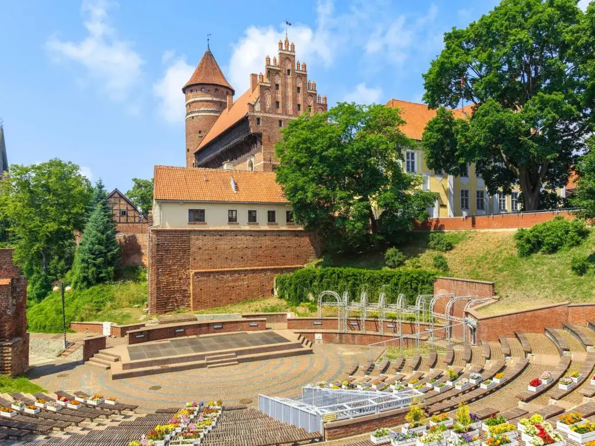Olsztyn co warto zobaczyć: amfiteatr i zamek z cegły, otoczone zielenią. Idealne miejsce na letnie wieczory.