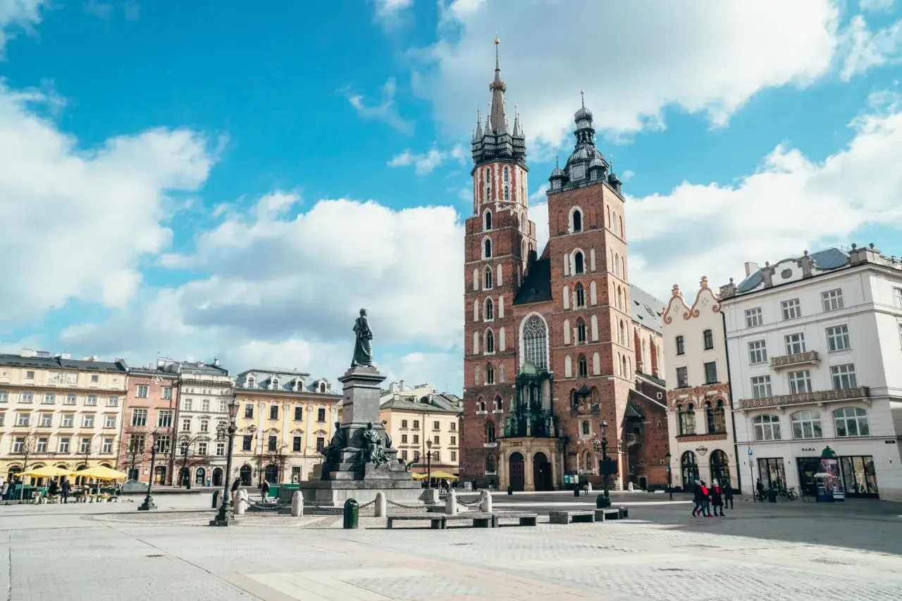 Rynek Główny w Krakowie, z Bazyliką Mariacką i pomnikiem Mickiewicza. Stare miasto Kraków tętni życiem pod błękitnym niebem.