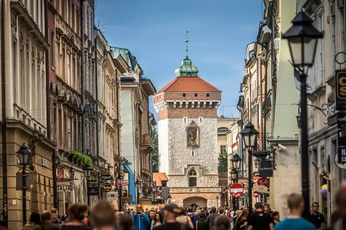 Tłum ludzi idzie ulicą w stronę zabytkowej Bramy Floriańskiej z charakterystyczną wieżą i czerwonym dachem.