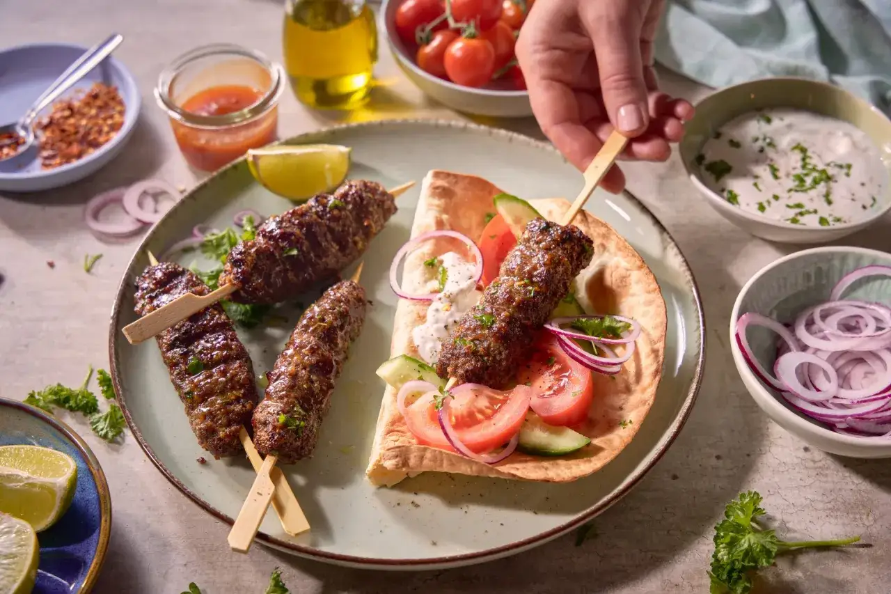 Pyszny kebab w Turcji na talerzu z dodatkami: pomidory, ogórek, cebula, sos i płaski chleb.