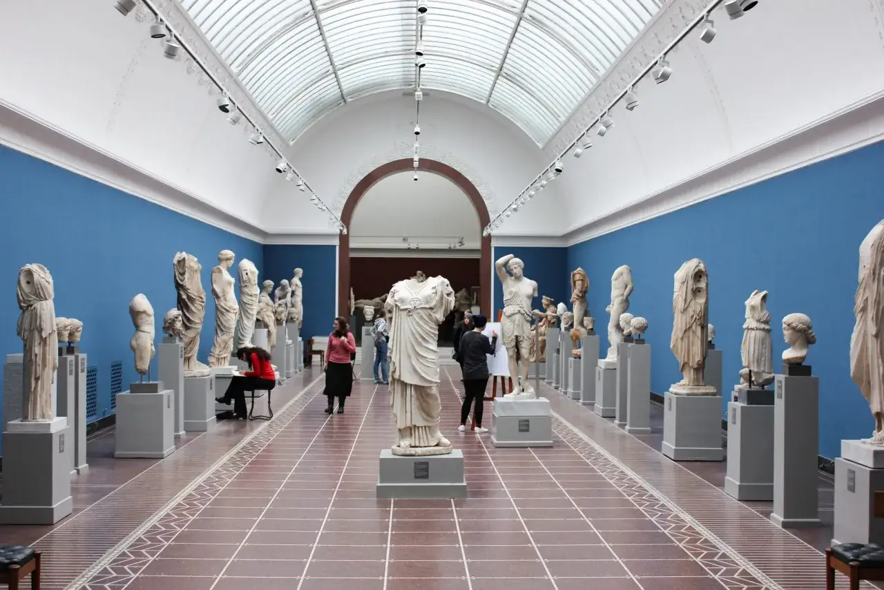 Wnętrze muzeum w Krakowie z rzeźbami antycznymi. Zwiedzający podziwiają dzieła sztuki, jedna osoba szkicuje.