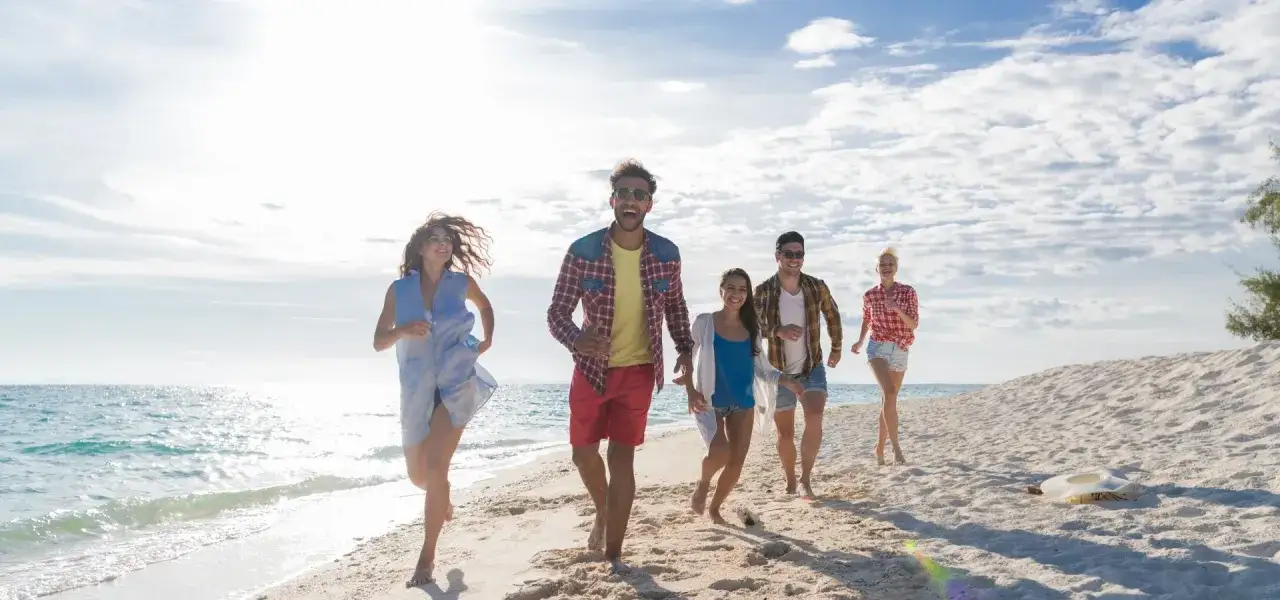 Radosna grupa przyjaci&oacute;ł biegnie po plaży, ciesząc się słońcem i morzem. Typowy Polak na wakacjach w pełni korzysta z wolności i beztroski.