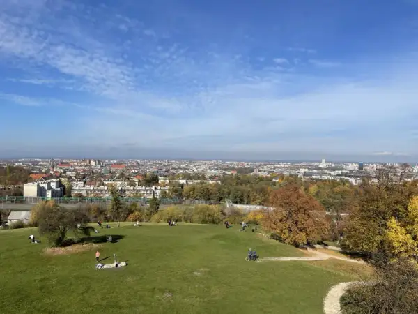 Jesienny dzień w Krakowie. Ludzie odpoczywają na zielonej trawie, a w tle rozciąga się panorama miasta.
