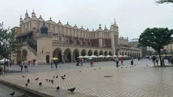 Deszczowy dzień na Rynku Głównym w Krakowie. Ludzie z parasolami spacerują, szukając schronienia w Sukiennicach lub kawiarniach. To świetny pomysł, co robić w Krakowie, gdy pada.