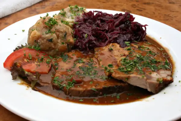 Pyszne jedzenie w Niemczech: pieczeń wieprzowa w sosie, kluski ziemniaczane, czerwona kapusta i pomidor.