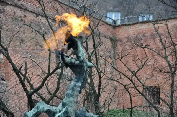 Pomnik smoka wawelskiego zieje ogniem na tle ceglanej ściany.
