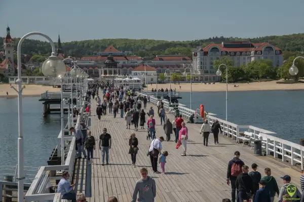 Spacer po molo w Sopocie, pełnym ludzi, to jedna z **nietypowych atrakcji Gdańska** i okolic. W tle widać plażę i zabytkowe budynki.
