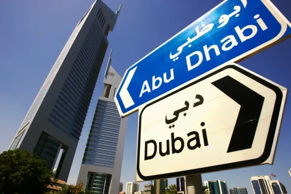 Znaki drogowe wskazują kierunek do Abu Zabi i Dubaju, na tle nowoczesnych wieżowców.
