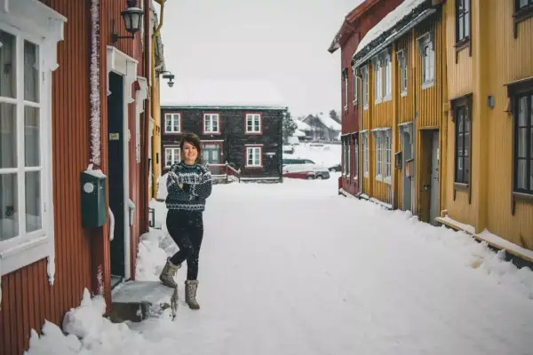 Uśmiechnięta kobieta w swetrze stoi na zaśnieżonej ulicy w Oslo zimą.