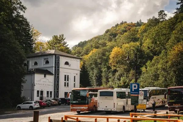 Autobusy czekają przed Starą Kruszarnią w Złotym Stoku. Jesienne drzewa otaczają parking.