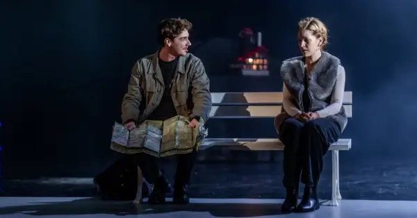 Para na ławce, mężczyzna z mapą, kobieta w futrzanej kamizelce. Scena z dramatu "Jelegnia Góra" pełna napięcia.