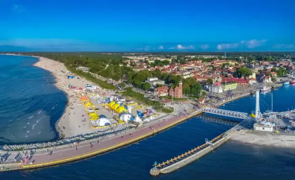 Ustecka plaża tętni życiem, pełna kolorowych namiotów i ludzi. W tle widać urokliwe miasteczko i port. To idealne ustka atrakcje dla każdego.