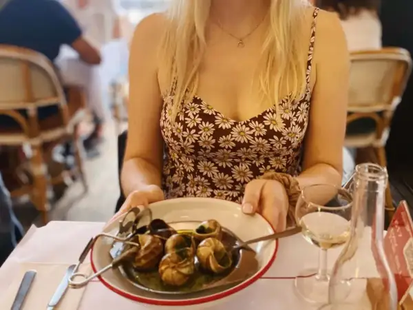 Paryż jedzenie: kobieta w letniej sukience serwuje ślimaki w restauracji, obok kieliszek białego wina.
