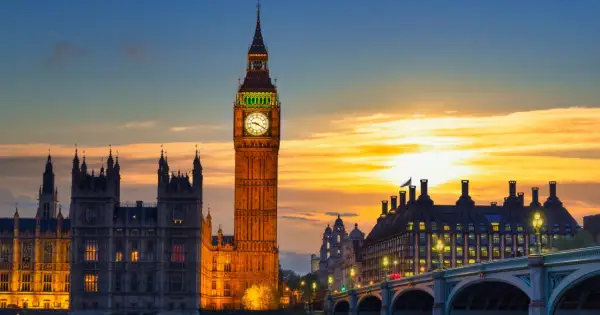 Wieża zegarowa Big Ben w Londynie o zachodzie słońca, z Parlamentem i mostem w tle.