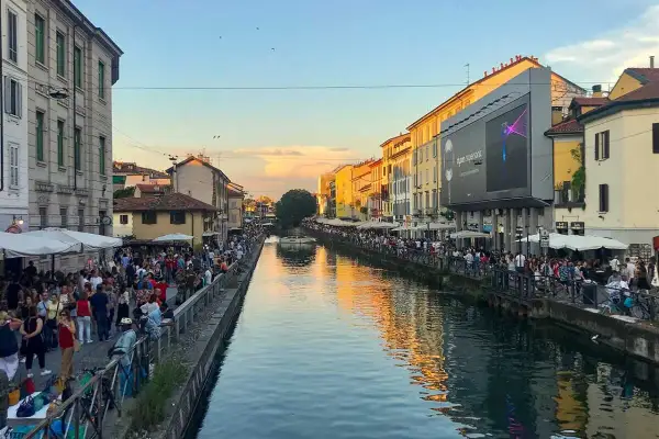Tętniące życiem Navigli w Mediolanie. Ludzie spacerują wzdłuż kanału, ciesząc się wieczornym słońcem i atmosferą.